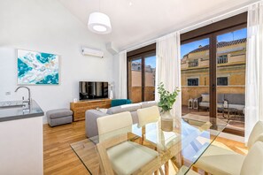 En moderne stue med et glasbord, grå sofaer, et fjernsyn og et stort vindue med gardiner.