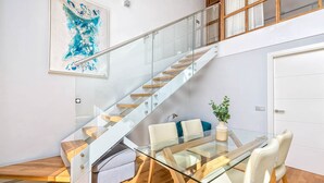 A modern interior with a glass staircase, a dining area with a glass table and chairs, and a white door.