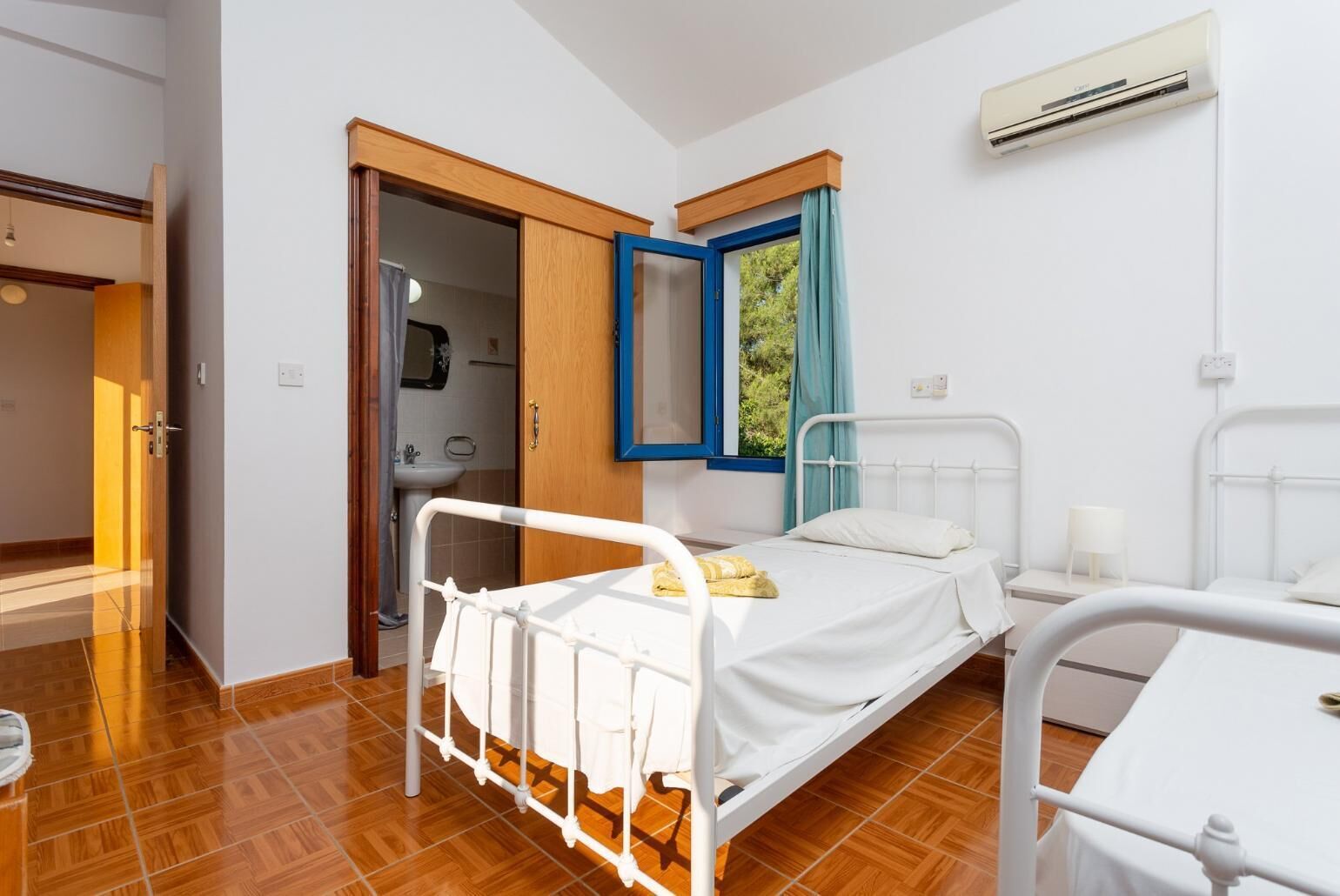 Une chambre avec un lit simple, une table de chevet, une fenêtre avec des rideaux bleus et un climatiseur fixé au mur.