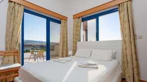 A hotel room with a large bed, two windows with blue frames, and a view of the landscape.