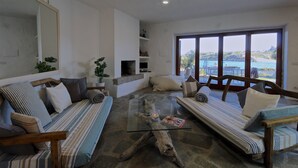 A living room with a glass coffee table, two sofas, a TV, and a large window with a view of the sea. - Maison Monte d'A Rena (La Maddalena)