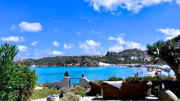 A beach with clear blue water, a rocky landscape, and a few people in the distance. - Maison Monte d'A Rena (La Maddalena)