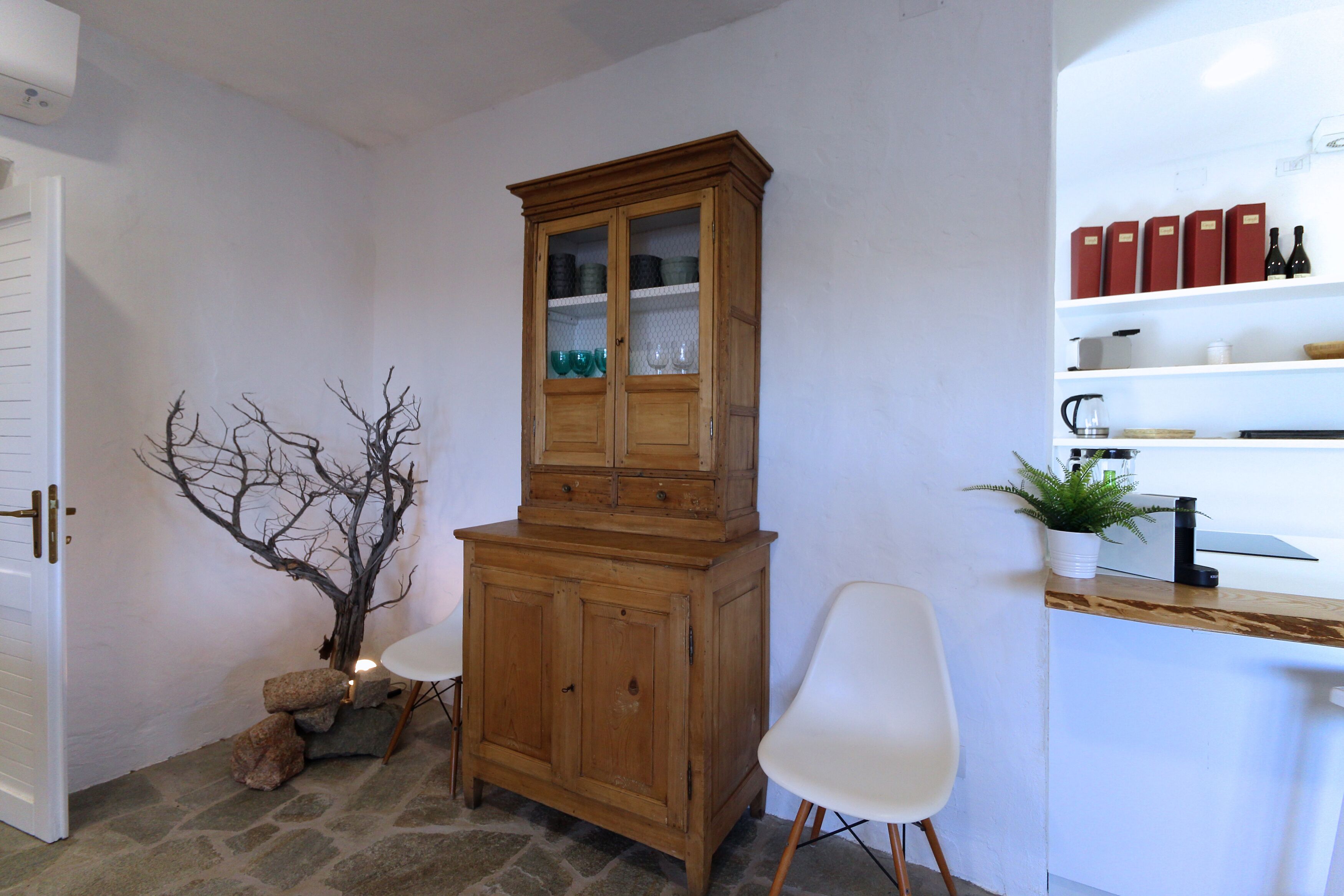 A wooden cabinet with glass doors, a white chair, and a small plant on a counter.