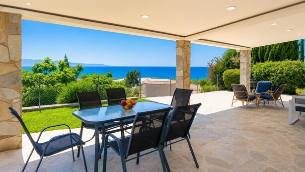 An outdoor patio with a table and chairs, a stone pillar, and a view of the sea. - Argaka Sunset Villa - Three Bedroom Villa, Sleeps 6 (Argaka)