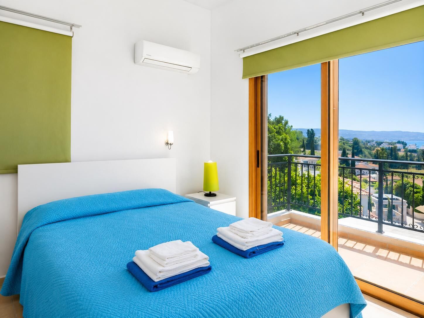 Un dormitorio con cama, mesita de noche, aire acondicionado, lámpara y balcón con vistas.