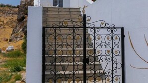 A white building with a metal gate and a staircase leading to a balcony with red flowers.