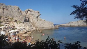 A rocky beach with clear water, umbrellas, and people swimming.