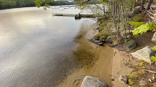 A calm lake with a dock extending into the water, surrounded by rocks and greenery.