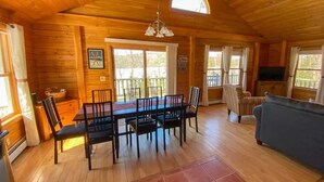A wooden cabin interior with a dining table, chairs, a sofa, and a TV.