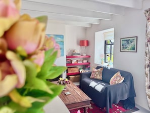 A living room with a sofa, a coffee table, a bookshelf, and a window. - Rock Cottage Self Catering Cottage (County)
