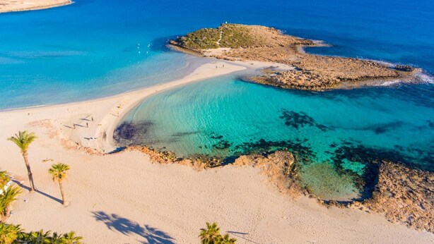 Una playa costera con aguas turquesas cristalinas, orillas de arena y afloramientos rocosos.