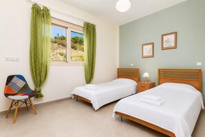 Une chambre avec deux lits, une chaise, une fenêtre avec des rideaux et une lampe sur une table de chevet.