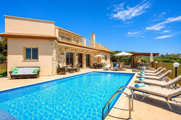 Une piscine avec des chaises longues, une maison en pierre et du mobilier d’extérieur.
