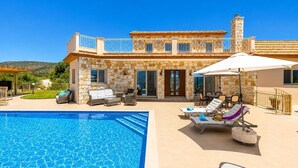 Una casa de dos pisos con piscina, mobiliario exterior y fachada de piedra.