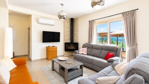Una sala de estar con un sofá, una mesa de centro, un televisor, una chimenea y vistas a través del ventanal.