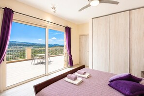 Un dormitorio con una cama grande, un balcón con vistas y un ventilador de techo.