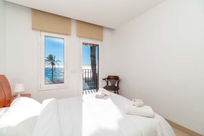 A hotel room with a bed, a chair, a lamp, and a view of the sea through a window. - Family Apartment Vistamar Beach (Vilassar de Mar)