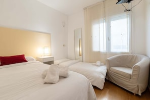 Une chambre d’hôtel avec deux lits, un oreiller rouge, une chaise blanche, une table de chevet avec une lampe, un miroir et une fenêtre avec des rideaux.