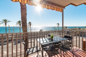 A balcony with a table and chairs, overlooking a beach with palm trees and the sea. - Family Apartment Vistamar Beach (Vilassar de Mar)
