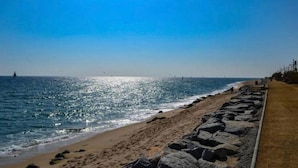 A beach with a rocky shoreline, a clear sky, and a sailboat in the distance. - Residential Costamar Playa, with swimming pools near Bcn (Cabrera de Mar)