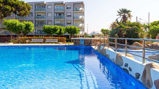 A swimming pool with a stone border, benches, and a building with balconies in the background. - Residential Costamar Playa, with swimming pools near Bcn (Cabrera de Mar)