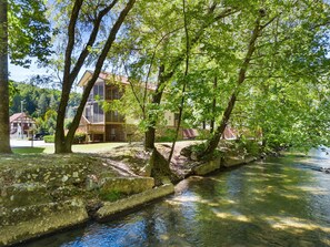 A riverside hotel with a stone bridge, surrounded by lush greenery and trees. - Chattahoochee River House 2 - Say Hello to Neighbors at the Helen Festhalle! (Helen)