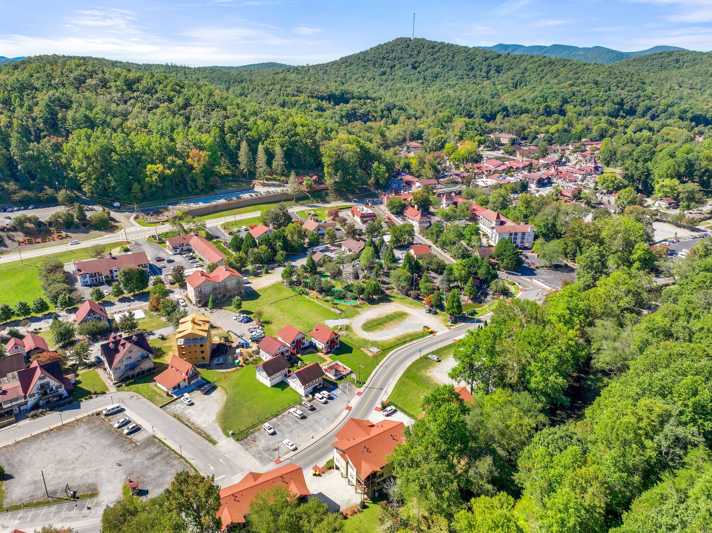 An aerial view of a small town with red-roofed houses, a central road, and surrounding greenery.