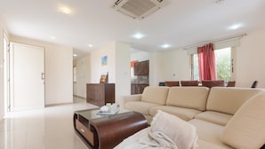 A spacious living room with a beige sofa, a wooden coffee table, and a kitchen area in the background.