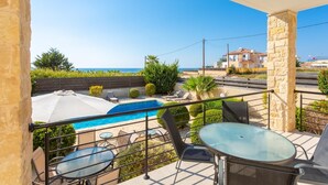 A balcony with a pool, outdoor seating, and a view of the sea.