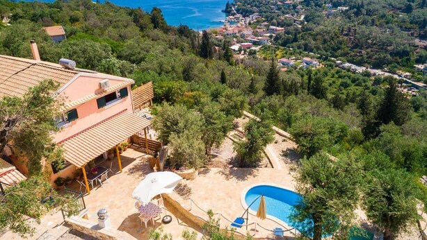 Eine Villa mit Swimmingpool, Sitzgelegenheiten im Freien und Blick auf das Meer und die umliegenden Hügel.