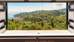 Ein Fenster mit Blick auf eine Küstenstadt, viel Grün und einen klaren Himmel.