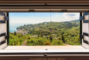A window with a view of a coastal town, greenery, and a clear sky.