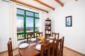 A dining area with a table set for four, a view of the landscape through green-framed windows, and a shelf with kitchen items.