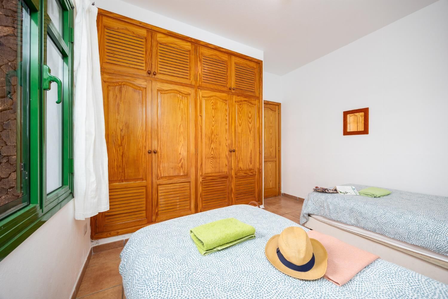 Ein Zimmer mit zwei Betten, einem Holzschrank, einem Fenster mit grünen Rollläden und einem kleinen, gerahmten Bild an der Wand.