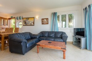 A living room with a leather sofa, a wooden coffee table, a TV, and a dining area with a table and chairs.
