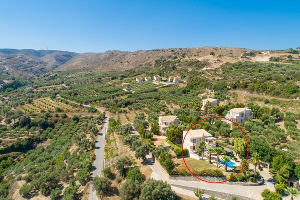 Vista aérea de una propiedad en una ladera con varias construcciones, un camino sinuoso y un área de piscina marcada en rojo.