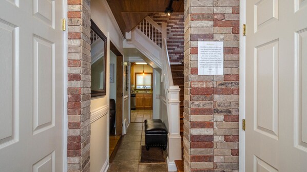 A hallway with a brick wall, a bench, and a staircase leading to a second floor.