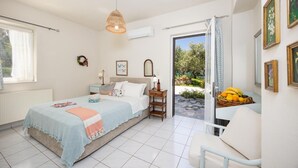 A bedroom with a bed, bedside table, lamp, and a view of the garden through an open door. - Villa Armi - Four Bedroom Villa, Sleeps 8 (Pirgos)