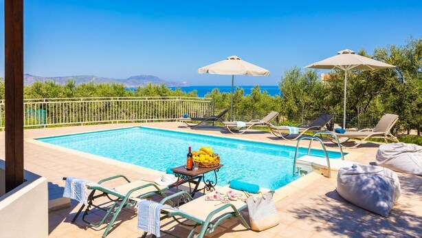 A poolside area with lounge chairs, umbrellas, and a table with drinks and fruits. - Villa Armi - Four Bedroom Villa, Sleeps 8 (Pirgos)