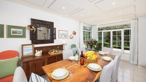 A dining area with a wooden table, chairs, and a view of the garden through large windows. - Villa Armi - Four Bedroom Villa, Sleeps 8 (Pirgos)