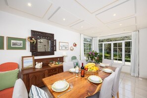 Un espace repas avec une table en bois, des chaises et une vue sur le jardin grâce à de grandes fenêtres.