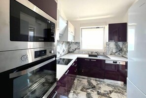 Kitchen features stainless steel appliances, a window above the sink, and dark-colored cabinets.