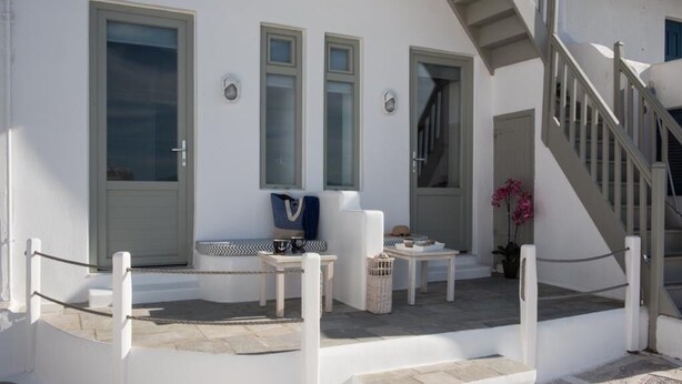 A white building with a staircase, a door, and a small table with items on it. - Christy Suites by Alpha Living (Mykonos)