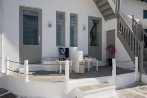 Un edificio blanco con una escalera, una puerta y una pequeña mesa con objetos encima.