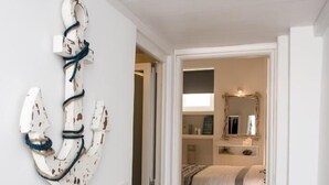 A hallway leading to a bedroom with a bed, a mirror, and a wall-mounted decorative anchor. - Christy Suites by Alpha Living (Mykonos)