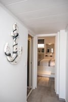 Un pasillo que conduce a un dormitorio con una cama, un espejo y una ancla decorativa en la pared.