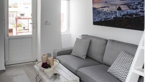 A modern living room with a grey sofa, a white chest of drawers, and a large landscape painting. - Christy Suites by Alpha Living (Mykonos)
