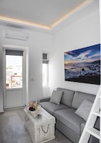 Una sala moderna con un sofá gris, un aparador blanco y un cuadro de paisaje grande.