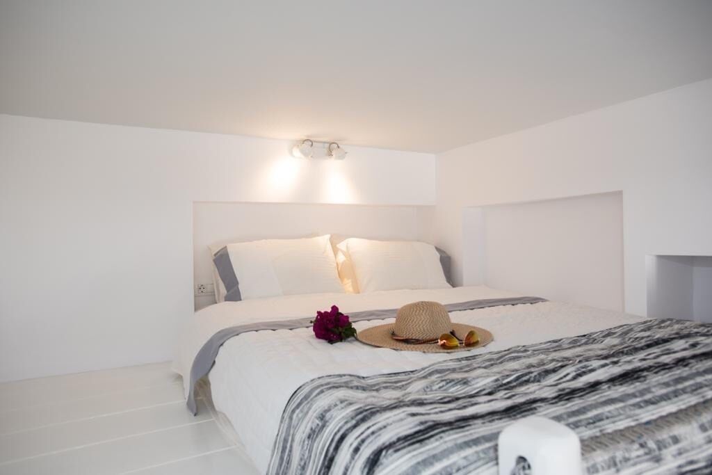 A modern bedroom with a large bed, white walls, and a ceiling light fixture.
