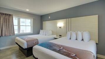 A hotel room with two beds, a large window with curtains, a wall-mounted light, and a wooden floor.